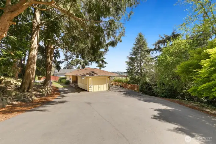 Generous paved driveway with room for multiple vehicles, attached garage, and pergola patio just beyond.