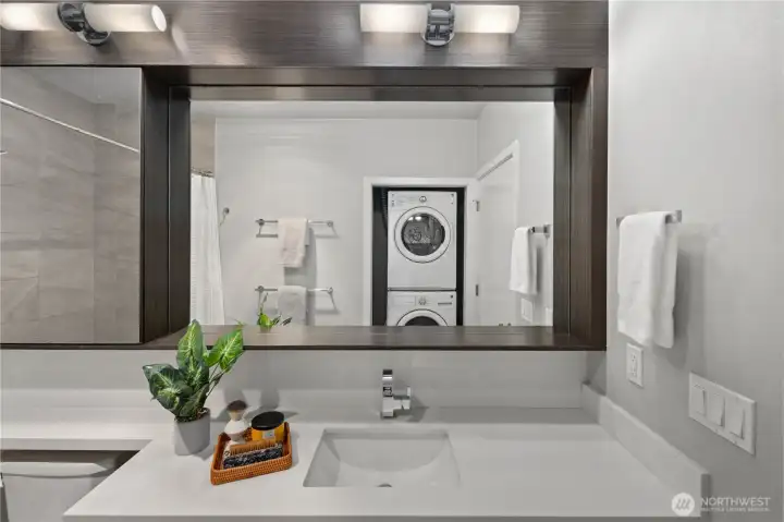 Refined and functional, this bathroom combines quartz-stone counters, designer fixtures, rich wood cabinetry, custom mirrored storage, and discreet front-load laundry.