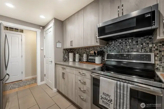 Beautifully updated kitchen with custom cabinetry, quartz countertops, sleek backsplash, stainless steel appliances + convection oven, ambient floor lighting, tile flooring, and pantry