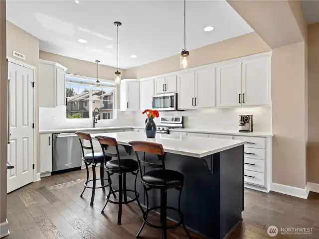 Featuring crisp white cabinetry, sleek quartz countertops, and a stunning dark island with bar seating, the space is ideal for both casual dining and entertaining.