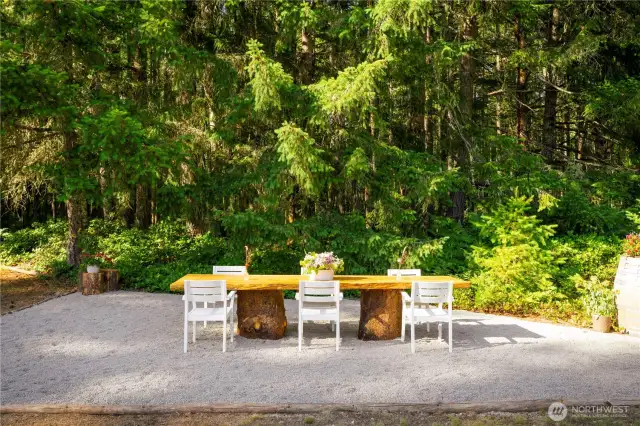 The outdoor dining area is surrounded by trees and the meadow and defined by logs from the property.