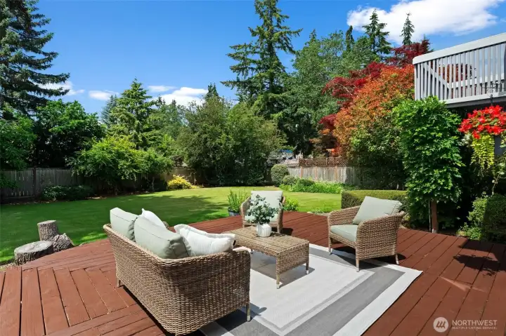 Generous outdoor living space overlooks a level lawn surrounded by established trees and plantings.