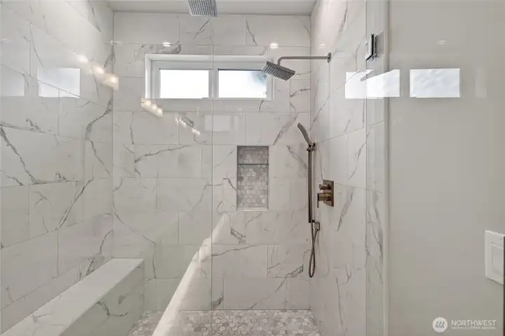 Primary bathroom's walk-in shower with three shower heads, built in bench and glass door.