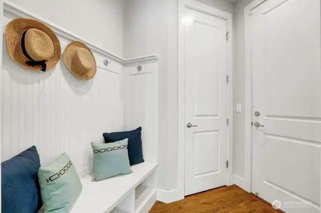 This well-appointed mudroom is fitted with a comfortable seating area, it provides a convenient spot to remove shoes or gear before stepping inside.  The cubbyholes and hanging area ensure organized storage for coats, bags, and everyday essentials, keeping clutter at bay. A separate closet adds even more functionality.  The door right leads to the garage which has been re-coated in epoxy offering a clean slate to the new owners