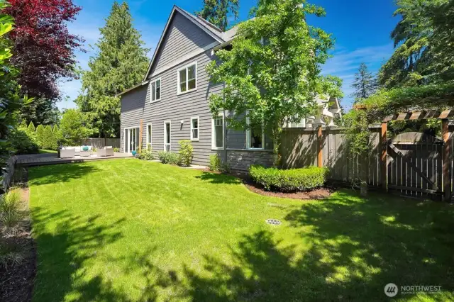 This beautiful view from the garden gate with arbor showcases the home beautifully, leading the eye toward the expansive grassy area and the Trex-like deck beyond