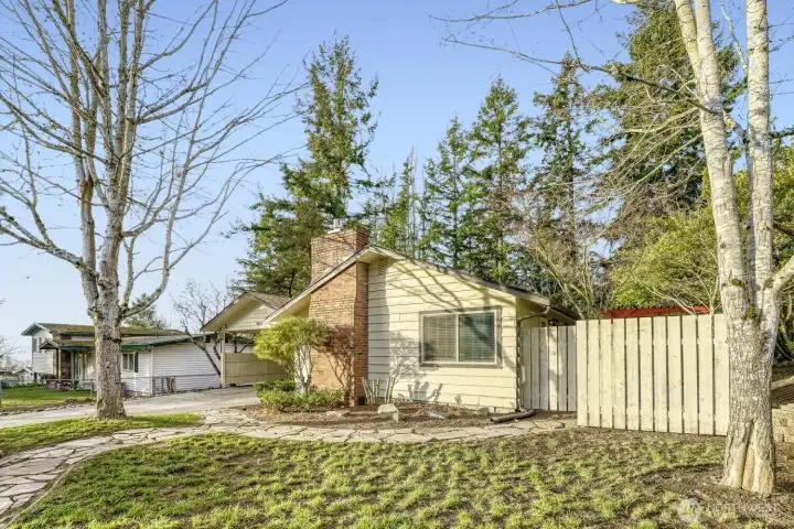 Fully fenced front yard featuring established landscaping, a flagstone pathway, and mature trees. The property boasts a newly installed roof, completed in 2026.