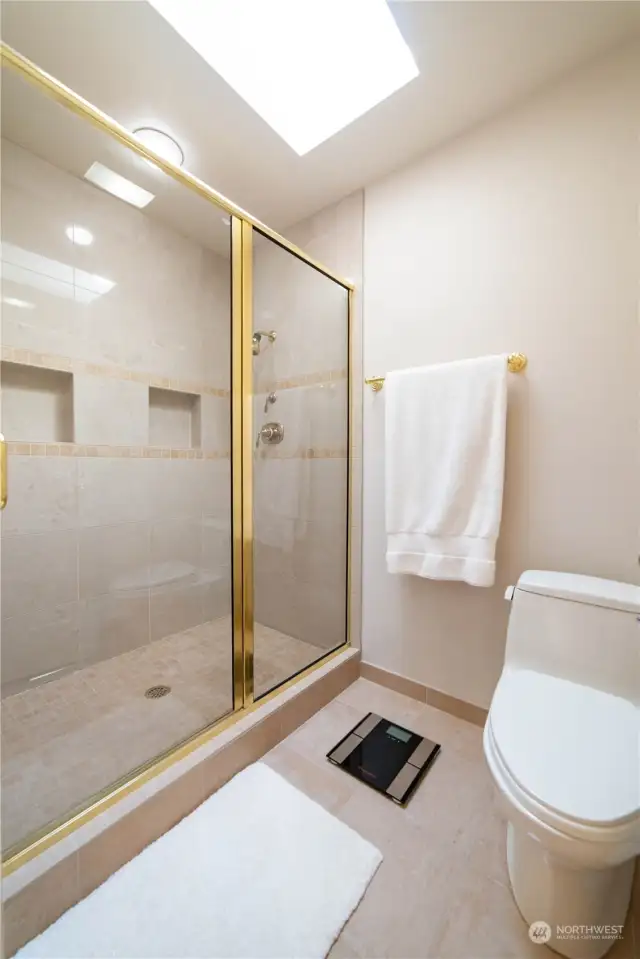 The primary bath suite's polished tile walk-in shower, which incorporates storage niches, recessed lighting and the skylight.  Notice also the vaulted ceiling.