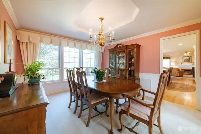 The formal carpeted dining room, with expansive windows overlooking the backyard and golf course, coved ceilin g with chandelier, and wall detailing including complimentary ceiling molding, chair rails and wainscoting.