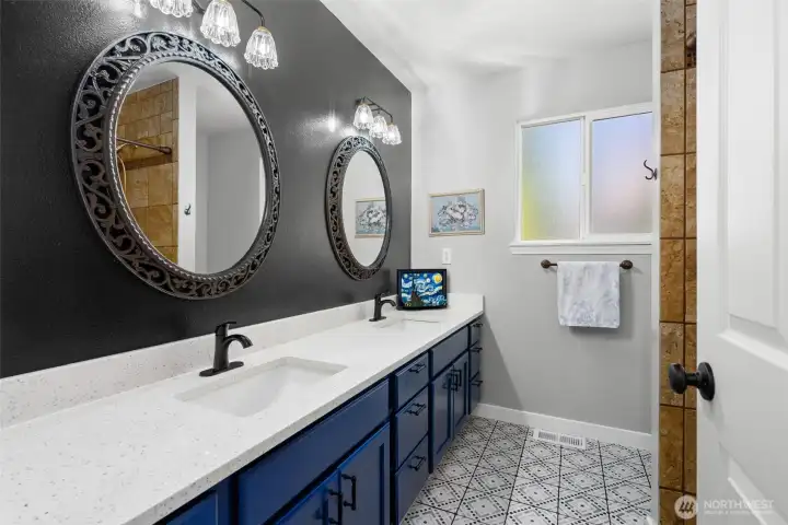 Newly renovated bath with dual vanity, cheerful tile floor and roomy tiled shower.