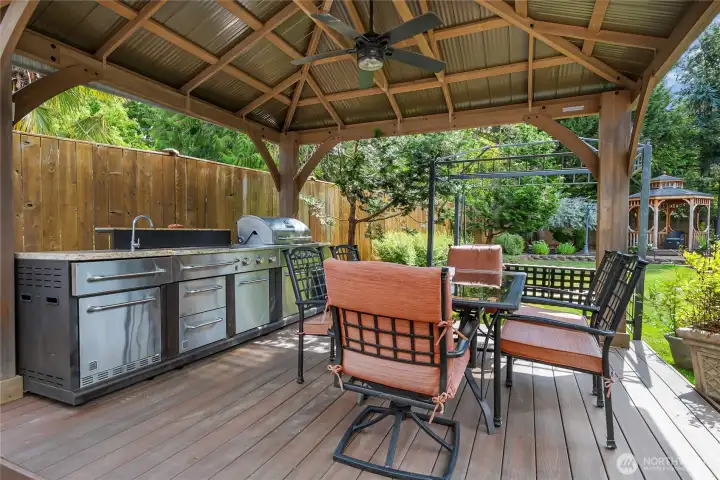 Outdoor entertaining is elevated with a covered outdoor kitchen featuring a built-in grill, sink, refrigerator and ample storage, all situated on a low maintenance Trex-deck. A remote controlled outdoor-rated ceiling fan provides added comfort, creating the perfect space to relax and entertain year-round. Outdoor entertaining is elevated with a covered outdoor kitchen featuring a built-in grill, sink, refrigerator and ample storage, all situated on a low maintenance Trex-deck. A remote controlled outdoor-rated ceiling fan provides added comfort, creating the perfect space to relax and entertain year-round.