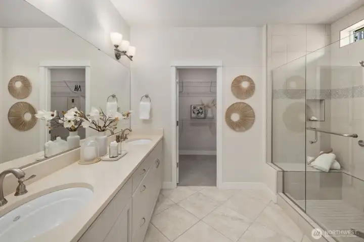 Primary bathroom with standup shower and bench. Dual vanities, and entrance to the walk in closet