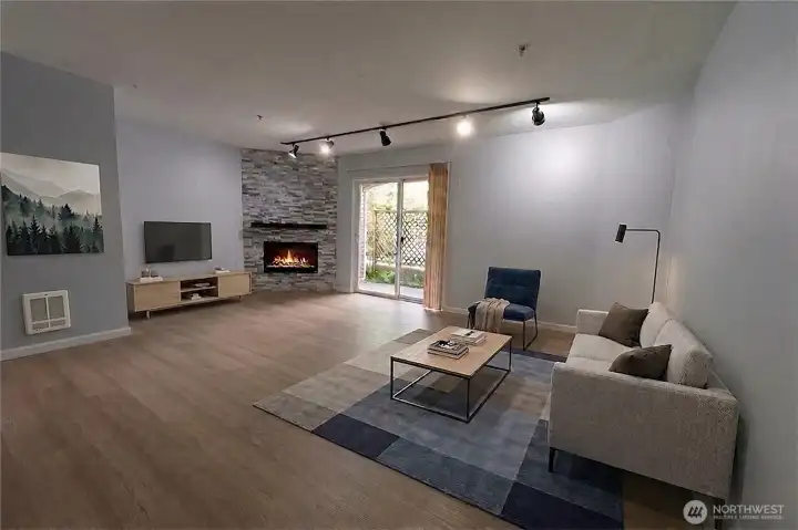 Spacious open-concept living room featuring luxury vinyl plank flooring, modern fireplace and private patio access
