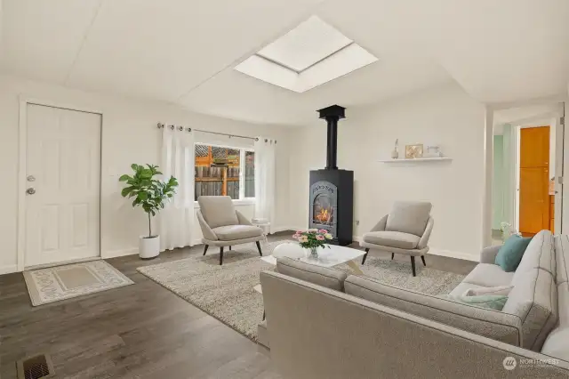 Formal living room with vaulted ceilings, skylight, laminate floors a a gas stove/fireplace.   Virtually staged photo.