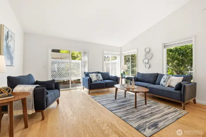 Dramatic living room with soaring vaulted ceilings. Engineered hardwood floors and gas fireplace. Slider opens to patio with privacy fence and manual awning