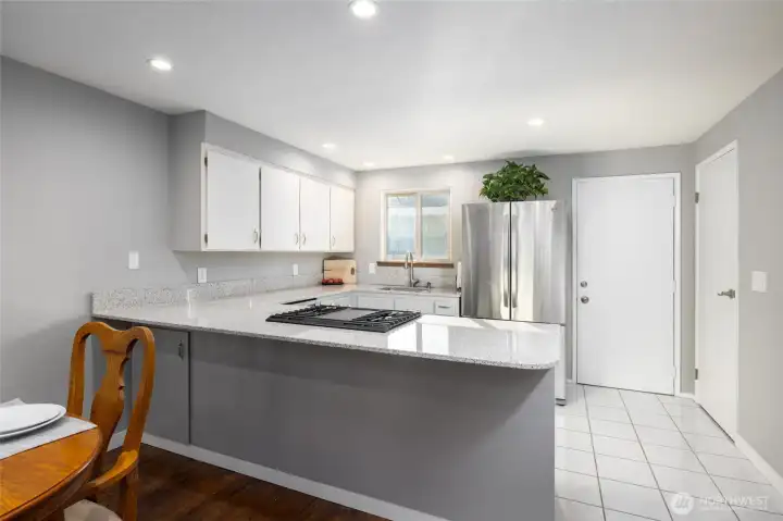 Open plan kitchen has quartz counters, gas range, stainless appliances. Door next to fridge leads to the enclosed private patio, door on the wall at right is the pantry.