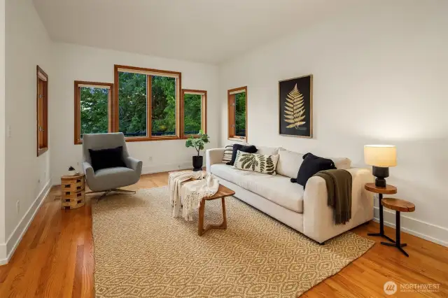 The living room offers a calm, grounded space with rich hardwood floors, clean white walls, and generous windows that frame the surrounding greenery. The layout is simple and flexible—perfect for quiet mornings with coffee or relaxed evenings with company. Natural textures and warm wood tones create a sense of comfort, while the abundant light gives the room an airy, uplifting feel. It’s a space that feels both modern and timeless, ready to adapt to any style of living.