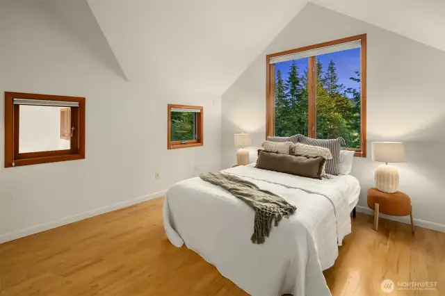 The primary bedroom upstairs offers a private, light-filled retreat with vaulted ceilings and tranquil views of the surrounding trees. Generous window placement brings in both morning and evening light, creating a calming atmosphere throughout the day. The clean, minimalist design pairs beautifully with the natural wood floors, offering a peaceful space to unwind. Whether you're waking up to birdsong or winding down after a long day, this room offers a sense of quiet and connection to nature that’s hard to find.