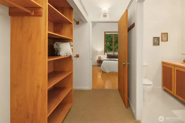 Upon entering the primary suite, you're greeted by a thoughtfully designed dressing area that blends function and warmth. Custom built-in shelving provides ample storage for clothing, linens, or personal items, while natural wood tones echo the calming aesthetic found throughout the home. To the right, the en suite bath is conveniently tucked away, maintaining flow and privacy. This transitional space offers both utility and a sense of retreat as you move into the bedroom beyond.