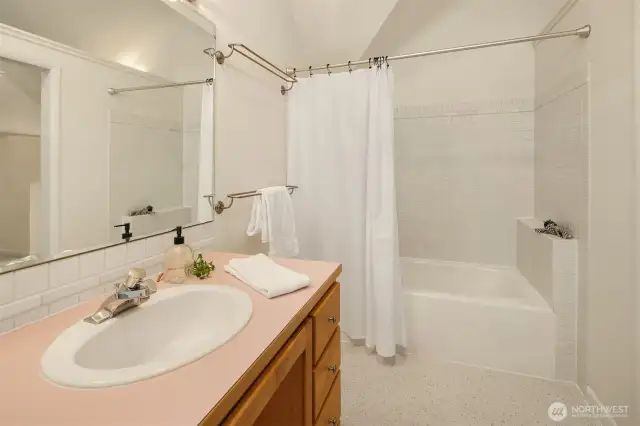The primary bath is clean, bright, and efficiently designed, offering everything you need in a calming, understated space. A full tub and shower combo is surrounded by classic white tile, while the wide vanity provides ample counter space and storage below. Soft neutral tones and vaulted lines add to the sense of airiness, making it feel open without being oversized. It's a practical, private en suite that complements the peaceful nature of the primary suite.