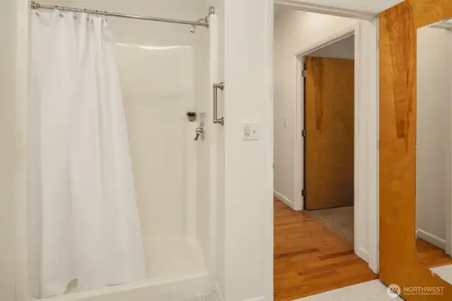 This view from the guest bath highlights its convenient central location—just steps from the main living areas and adjacent to both main floor guest bedrooms. The walk-in shower is a practical feature for guests of all ages, and the layout ensures easy access without sacrificing privacy. Thoughtful design and clean finishes make this space both functional and welcoming for everyday use or visiting family and friends.