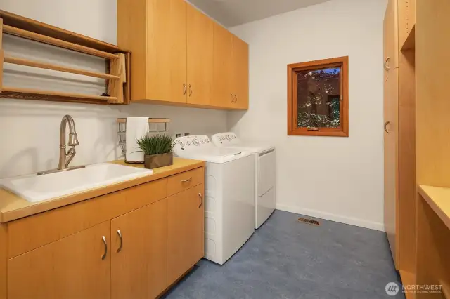 This well-appointed laundry room serves as a functional transition between the kitchen/pantry area and the attached two-car garage. Thoughtfully designed with ample cabinetry, a deep utility sink, and counter space for folding or prep, it makes daily tasks more efficient and organized. A window brings in natural light, while built-in hanging racks and storage cubbies add flexibility. Whether you're managing laundry, unloading groceries, or gearing up for the day, this space keeps everything within reach and out of sight.