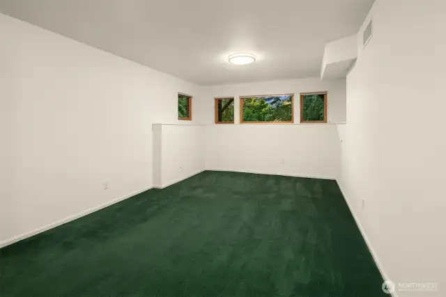 Located on the lower level, the fourth bedroom offers a quiet and private retreat with peaceful views of the surrounding trees through a row of high-set windows. The room is generously sized and filled with natural light, making it a versatile space for guests, a home office, or a creative studio. Its separation from the main living areas adds to the sense of privacy and flexibility.