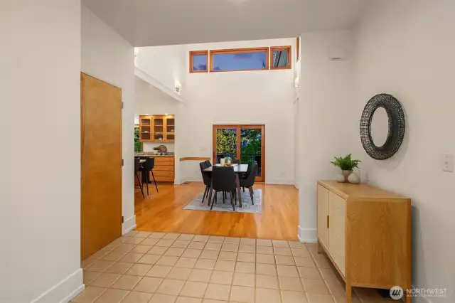 The entryway makes a welcoming first impression with its high ceilings, clean lines, and natural light filtering through upper transom windows. The tile flooring offers durability and an easy transition into the warm hardwoods beyond. From the moment you step inside, you get a sense of openness and flow—your eye is drawn through the dining area and out to the greenery beyond. It's a space that immediately feels calm, intentional, and connected to the home's overall design language.