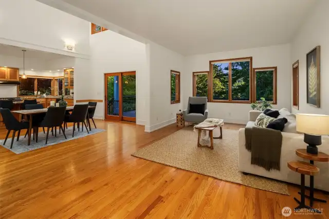 This open main living area brings together kitchen, dining, and living spaces in a warm, cohesive flow—ideal for both entertaining and everyday comfort. Generous windows frame the surrounding greenery and bring in soft natural light, while the hardwood floors and simple trim create a timeless, Northwest aesthetic. A sliding door off the dining area leads to the back deck, extending the living space outdoors. Whether you’re hosting guests or enjoying a quiet evening at home, the layout feels both open and grounded, with clear connection to the natural setting just beyond.