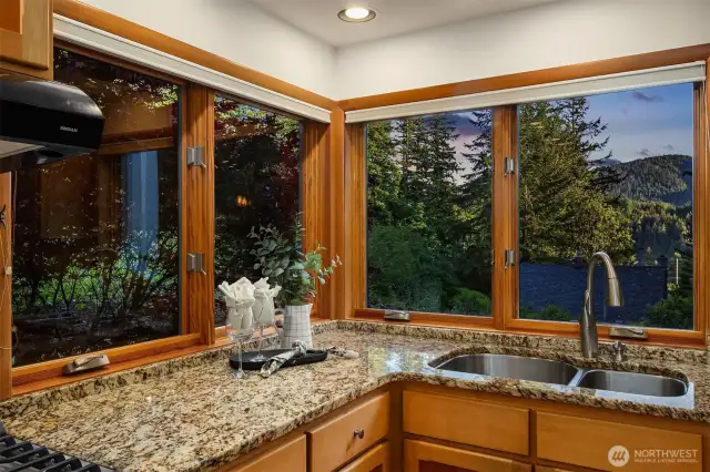 One of the standout features of this home is the kitchen's stunning corner window, offering sweeping views of the surrounding evergreens and foothills. Whether you're washing up or preparing a meal, you're treated to a peaceful, tree-filled backdrop with evening light filtering through. It’s a daily reminder of the natural beauty that surrounds 4714 Willis Street—just minutes from Lake Padden and the trail systems of Galbraith and Blanchard Mountains. This view connects the indoors with the outdoors in a way that feels distinctly Bellingham.