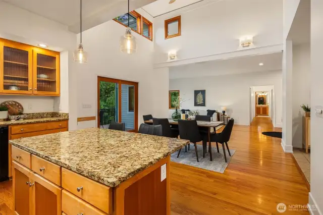 From the kitchen island, the home opens beautifully into the dining and living areas, creating a seamless flow for entertaining and everyday living. Vaulted ceilings and clerestory windows add volume and natural light, while the hardwood floors carry warmth throughout the space. French doors lead to the back deck, offering an easy indoor-outdoor connection. This layout is both inviting and functional, with sightlines that keep the heart of the home connected—ideal for gatherings, family meals, or simply enjoying the peaceful surroundings.