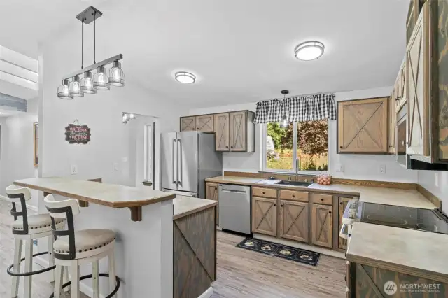 Rustic charm meets modern convenience in this beautifully updated kitchen featuring custom barn-style cabinetry, stainless steel appliances, a French door refrigerator, and a smooth electric cooktop with built-in air fry capability. The spacious layout includes a breakfast bar with designer pendant lighting—perfect for casual meals or entertaining guests. A large window above the sink brings in abundant natural light and offers a lovely view of the front yard. At the heart of the kitchen is a top-of-the-line, chef-grade sink—perfect for meal prep, washing large cookware, and making everyday kitchen tasks a breeze.