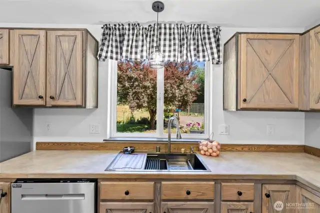 Enjoy peaceful views of the front yard and vibrant seasonal color through the large picture window above the kitchen sink. This space features a chef-grade workstation sink complete with integrated accessories—perfect for rinsing, chopping, and prepping all in one place. Surrounded by rustic barn-style cabinetry and generous counter space, this functional hub combines charm and convenience. Natural light pours in, creating a bright, cheerful atmosphere for everyday living and entertaining.