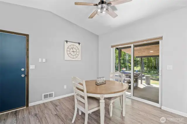 Bright and airy dining area with vaulted ceilings, modern ceiling fan, and large sliding glass doors that open directly to the covered patio—perfect for seamless indoor-outdoor living. The space is ideal for casual dining, game nights, or morning coffee with forest views. Natural light pours in, highlighting the luxury vinyl plank flooring and neutral color palette that pairs well with any decor style. Whether hosting or enjoying a quiet meal at home, this flexible dining space blends comfort, style, and function.
