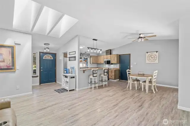 Expansive great room layout with vaulted ceilings, triple skylights, and an abundance of natural light. This open-concept space seamlessly connects the living, dining, and kitchen areas, creating an airy and inviting environment perfect for entertaining or everyday living. Luxury vinyl plank flooring flows throughout, while modern lighting and bold accent doors add style and personality. From the cozy coffee bar to the extended breakfast counter, every detail of this home balances comfort, charm, and functionality in a bright, well-designed floorplan.