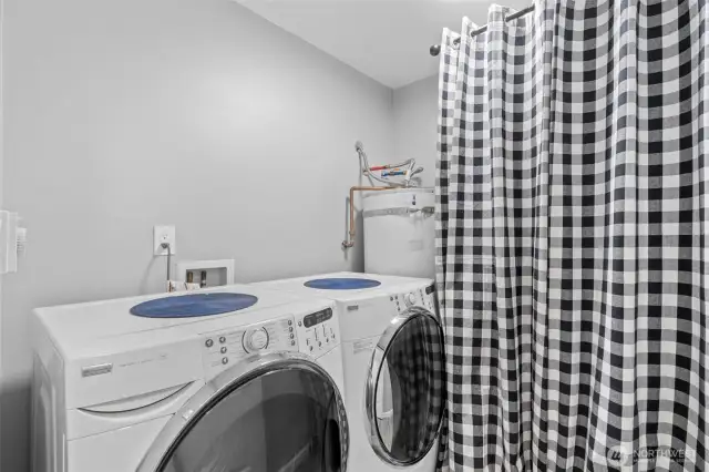 Functional and efficient, the utility room includes a front-loading washer and dryer, an electric hot water heater, and hidden shelving behind the curtain for all your storage needs.
