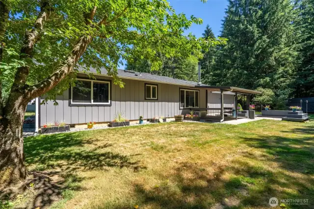 Peaceful backyard retreat, dappled sunlight, and a covered patio ideal for year-round outdoor living. The level lawn is perfect for hosting BBQs, lounging in the shade, or playing catch on sunny afternoons. Thoughtful landscaping includes flower beds, decorative planters, and a gravel border for low-maintenance beauty. The extended patio and built-in seating area create the perfect setting for outdoor dining, evening fires, or quiet mornings with coffee and birdsong. Embrace the lifestyle of private, country living with space to relax, garden, and unwind.