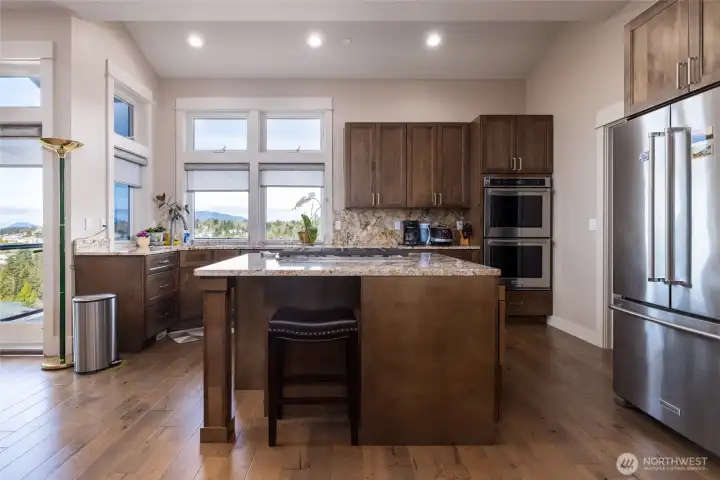 Custom kitchen with seating at island, gas range, double wall ovens and french door style refrigerator. Door to left provides access to the deck.