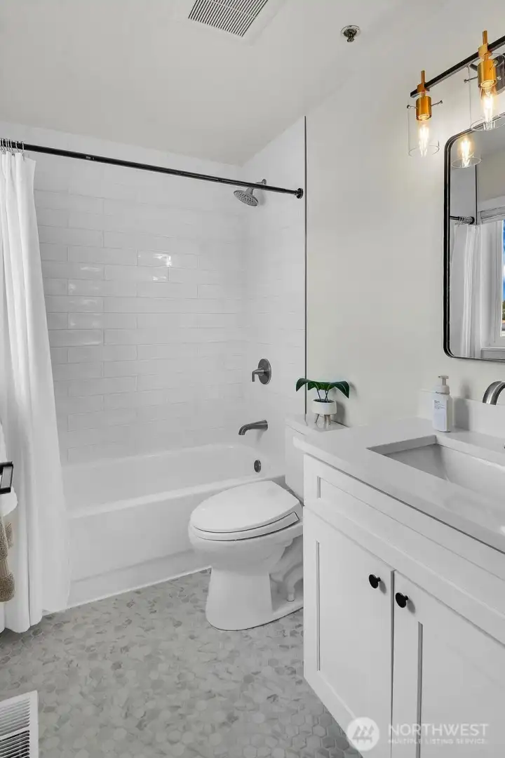 Updated bathroom with modern vanity, stylish lighting, and classic subway tile tub/shower surround.