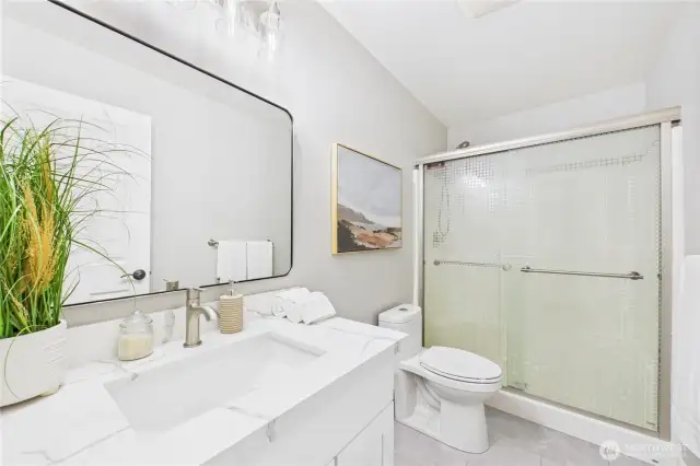 This stylish secondary bathroom features modern finishes, a quartz vanity, and a glass-enclosed shower/tub combo with privacy glass. Ideal for guests or family with a fresh, modern vibe.