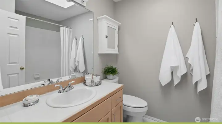 There is a full hall bath with a skylight vinyl flooring and tile counters.
