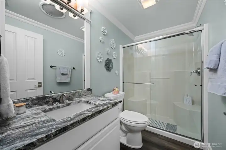 Well-appointed guest bathroom with granite vanity and glass-enclosed shower.
