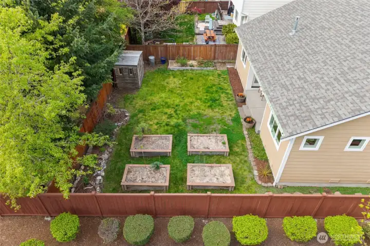 THE BACK YARD | This level back yard with raised garden beds is fully fenced and features a charming wood shed for convenient storage.