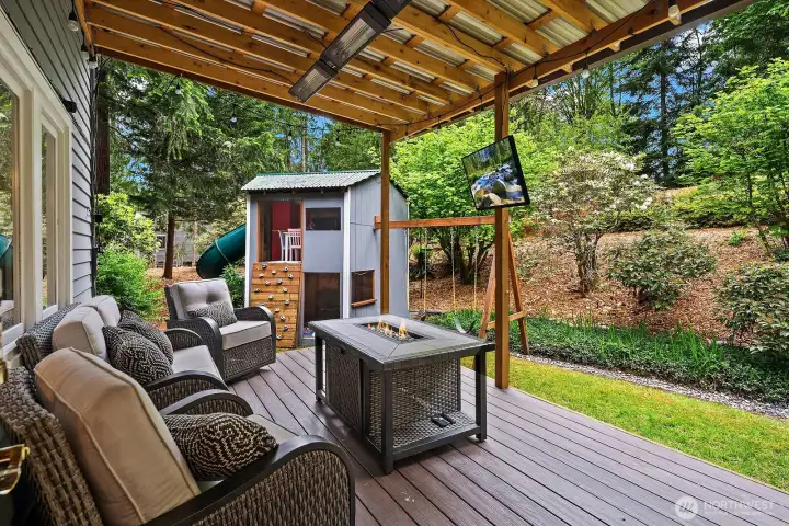 The beautifully designed covered deck offers a perfect outdoor living space with comfortable seating, a fire feature, and a serene backdrop of mature landscaping and lush greenery. The beautifully designed covered deck offers a perfect outdoor living space with comfortable seating, a fire feature, and a serene backdrop of mature landscaping and lush greenery.