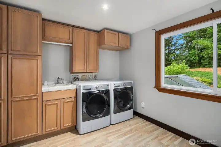 The generously sized laundry room features warm wood cabinetry, full-size washer and dryer, and a bright window, combining everyday practicality with the quality finishes found throughout the home. The generously sized laundry room features warm wood cabinetry, full-size washer and dryer, and a bright window, combining everyday practicality with the quality finishes found throughout the home.