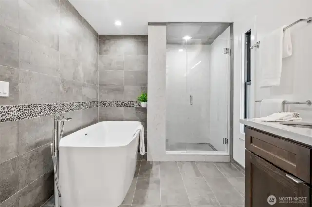 Unwind in style with this beautifully appointed primary bath, showcasing a luxurious freestanding soaking tub with a Hansgrohe fixture and a walk-in shower. Notice the beautifully crafted accent tile work that enhances the entire primary bathroom, adding a touch of elegance and artistry.