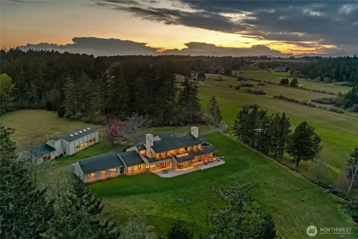 Dramatic sunset aerial showcasing the illuminated estate across expansive lawns, highlighting architectural scale and exceptional privacy within 63± acres.