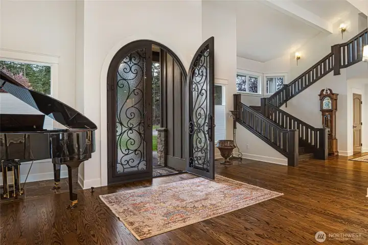 Impressive arched iron and glass entry doors open to soaring ceilings, rich hardwood floors, and a dramatic staircase with custom railing.