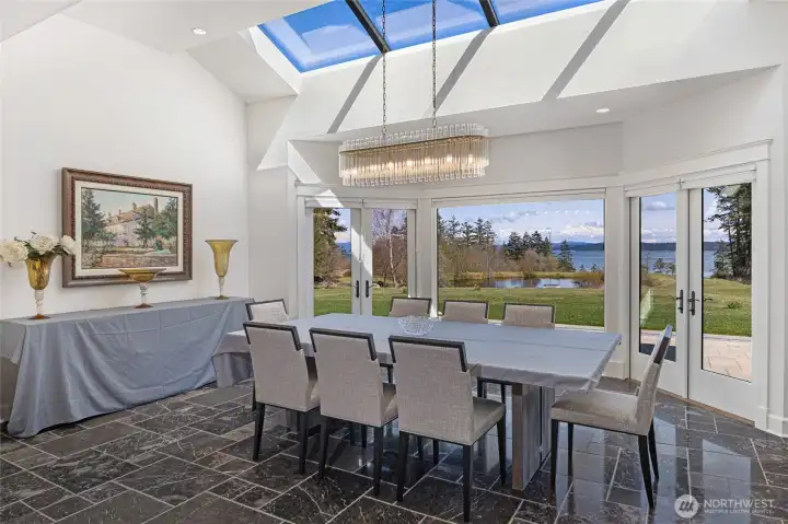 Light-filled formal dining room with skylight, modern chandelier, and expansive windows framing pond and water views.