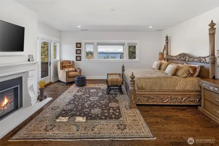 Spacious primary suite featuring gas fireplace, hardwood floors, private deck access, and expansive windows capturing panoramic San Juan Channel views.