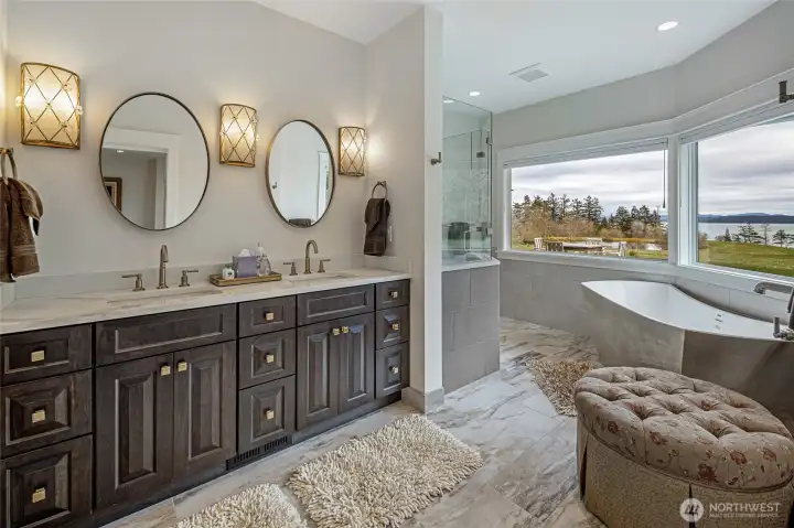 Spa-inspired primary bath with dual vanity, marble tile flooring, freestanding soaking tub, and panoramic water views toward the San Juan Channel.